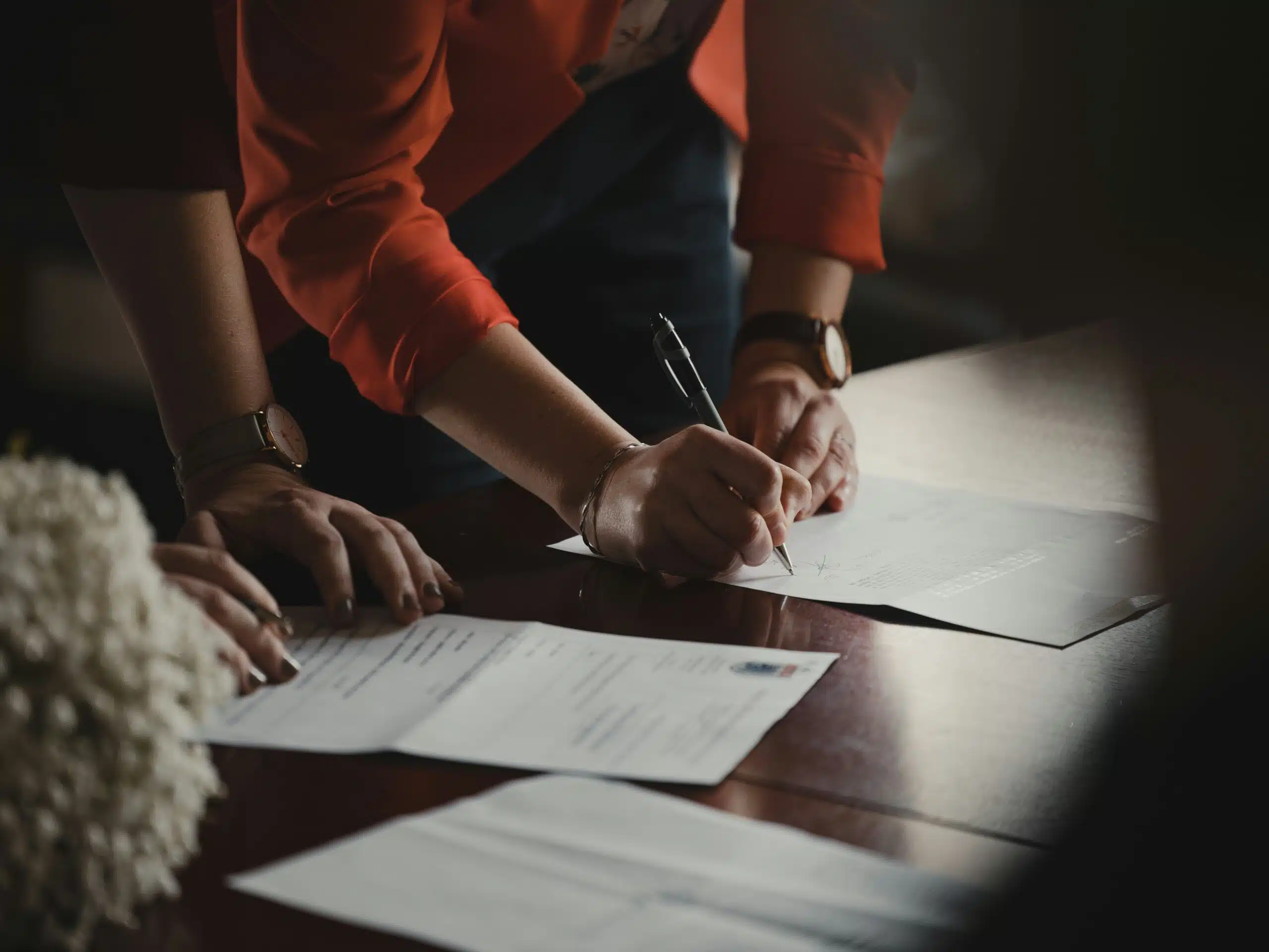 Person signing official documents on a wooden table, symbolizing the importance of securing local permits before placing rental tents.