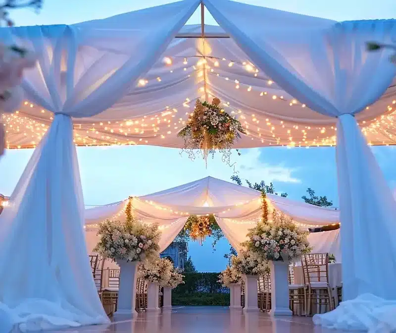 under a canopy of twinkling lights, a luxurious white tent stands elegantly adorned with flowing drapes and floral arrangements, ready for a charity gala.