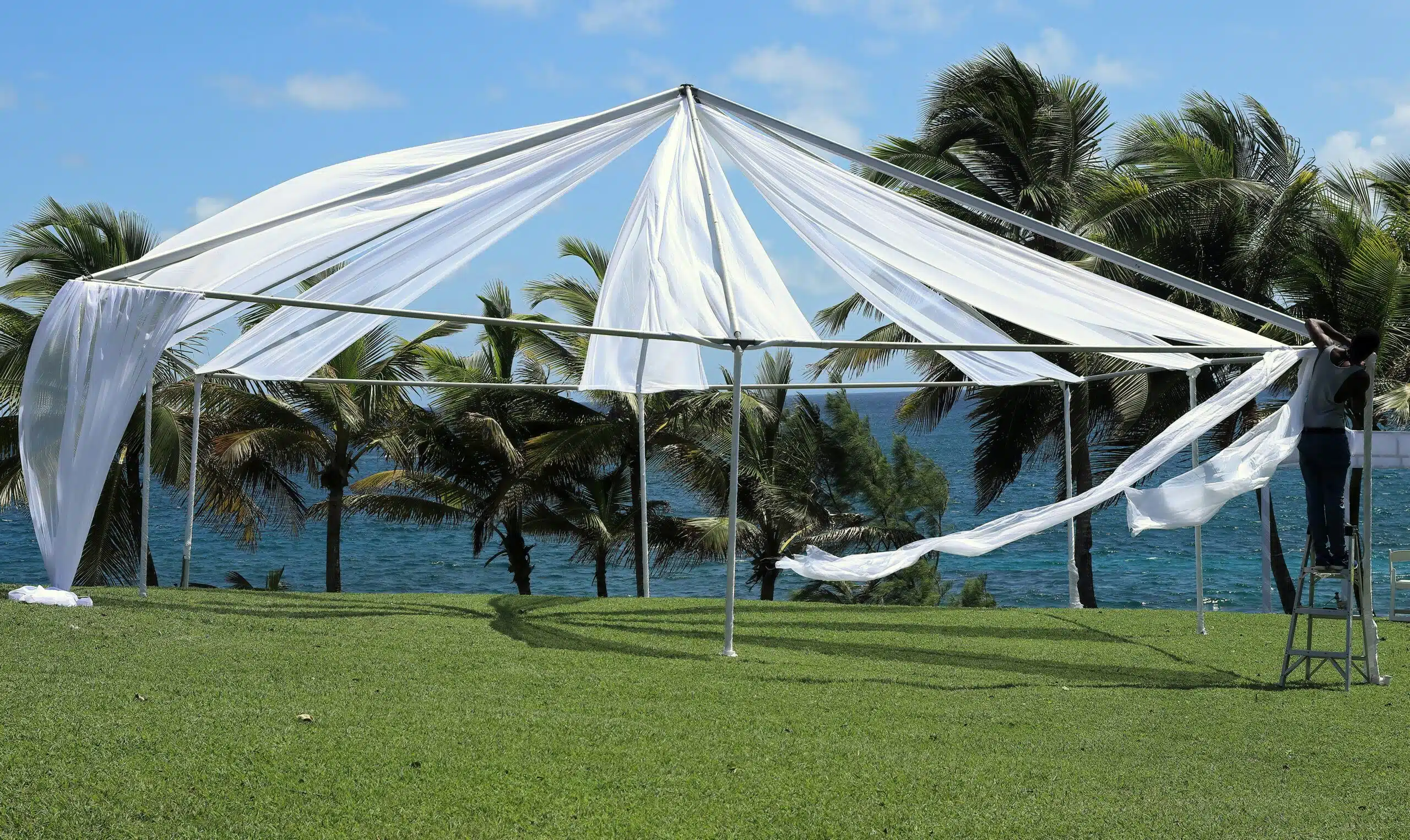 A breezy white tent frame being assembled on a seaside lawn, streamlining setup for a scenic outdoor event.