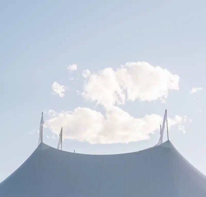 The top of a white canopy tent with clouds in the sky