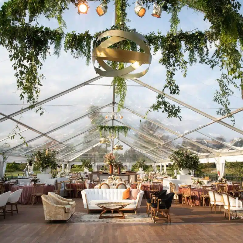 transparent event tent with golden hanging lights and greenery