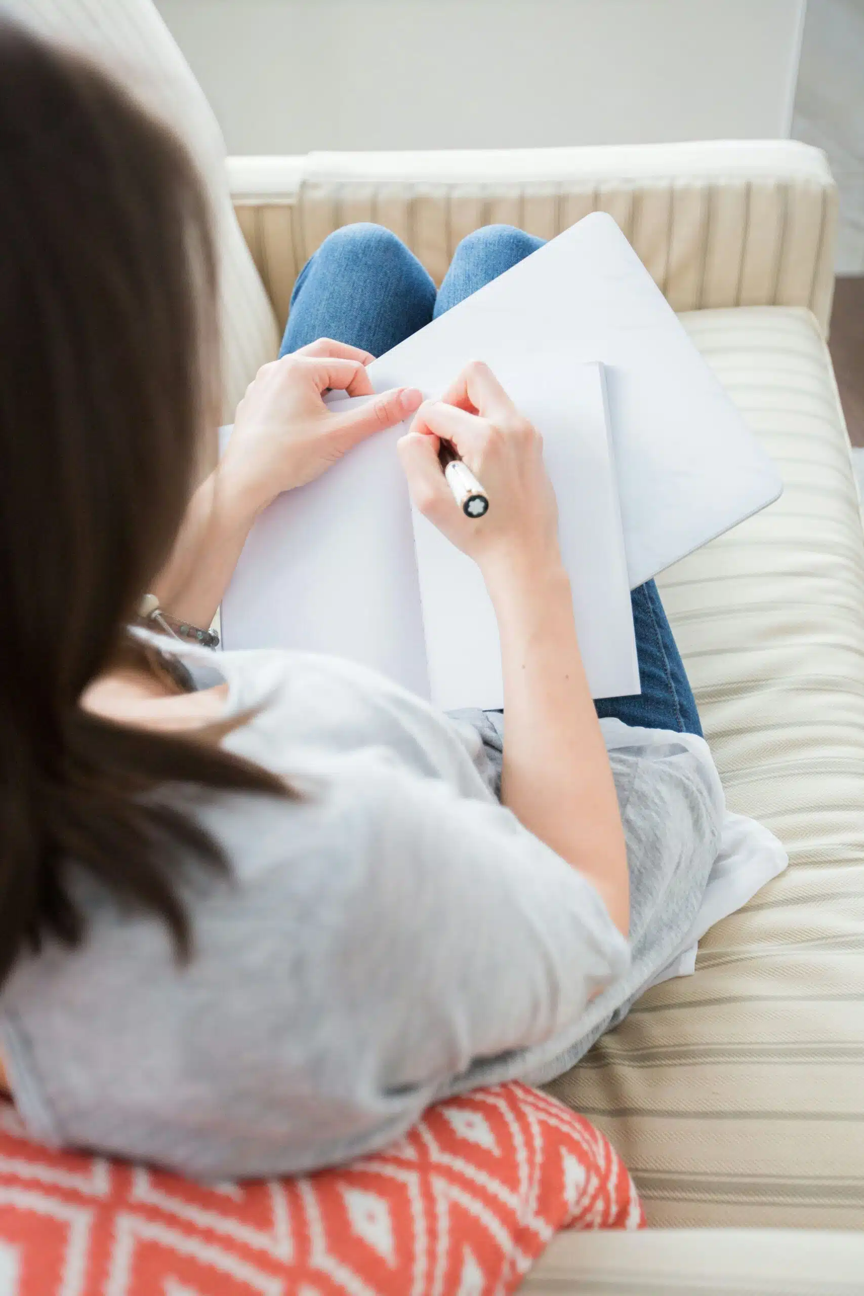 A person sitting comfortably on a couch, writing in a notebook while planning event details.