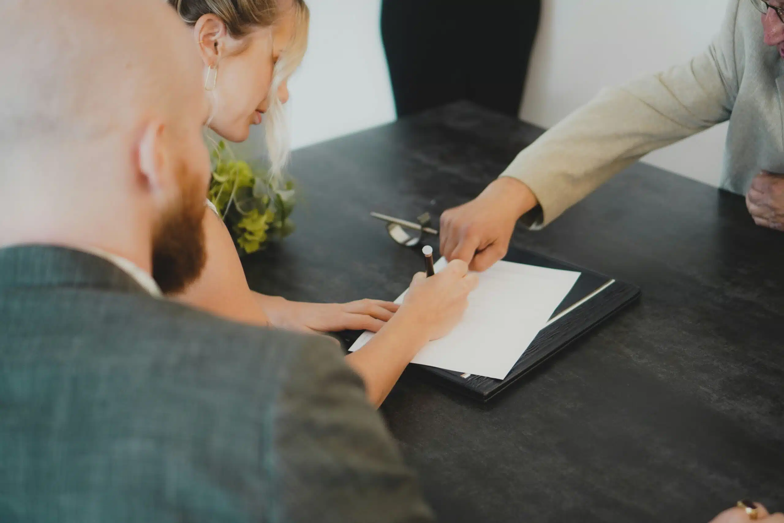 A person signing a contract at a table while discussing terms with two others, emphasizing the importance of understanding rental pricing.