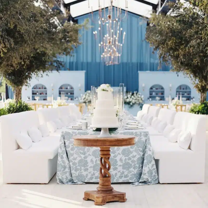 Elegant wedding tent interior with white cake display, modern chandeliers, and symmetrical seating.