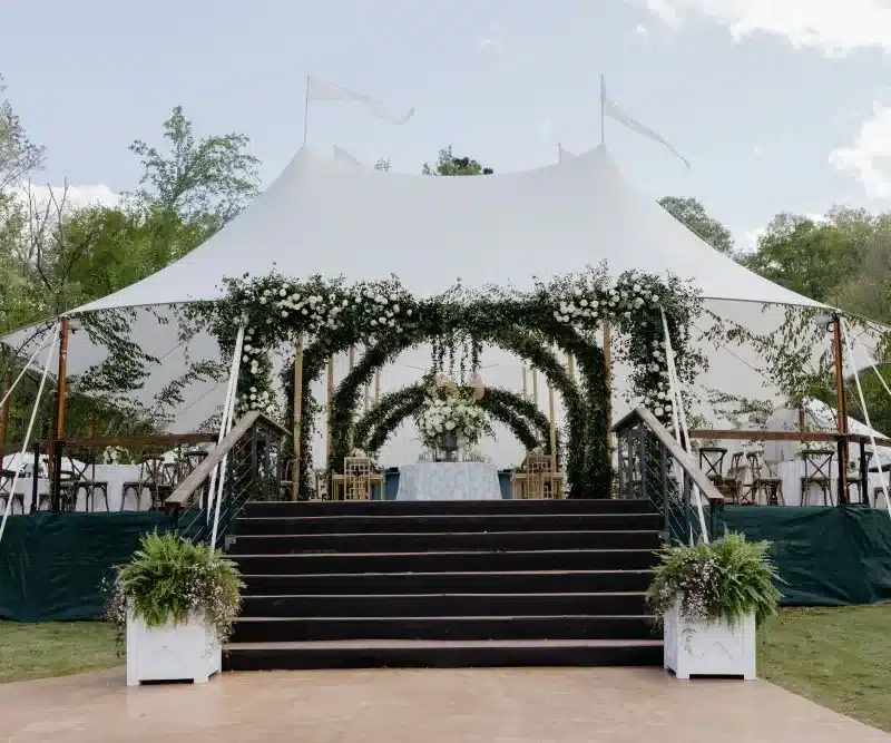 Elegant sailcloth wedding tent with floral arch entrance and tiered stage access.