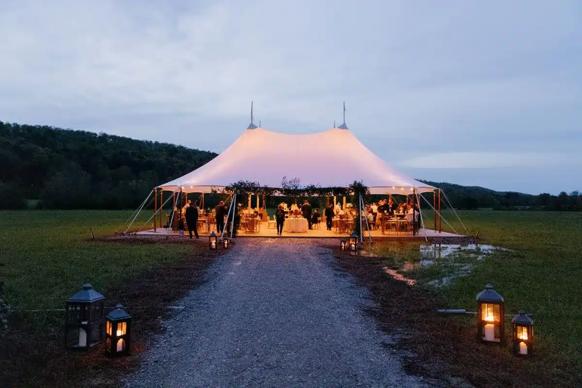 Sailcloth tent lit from within at twilight, pathway lined with lanterns