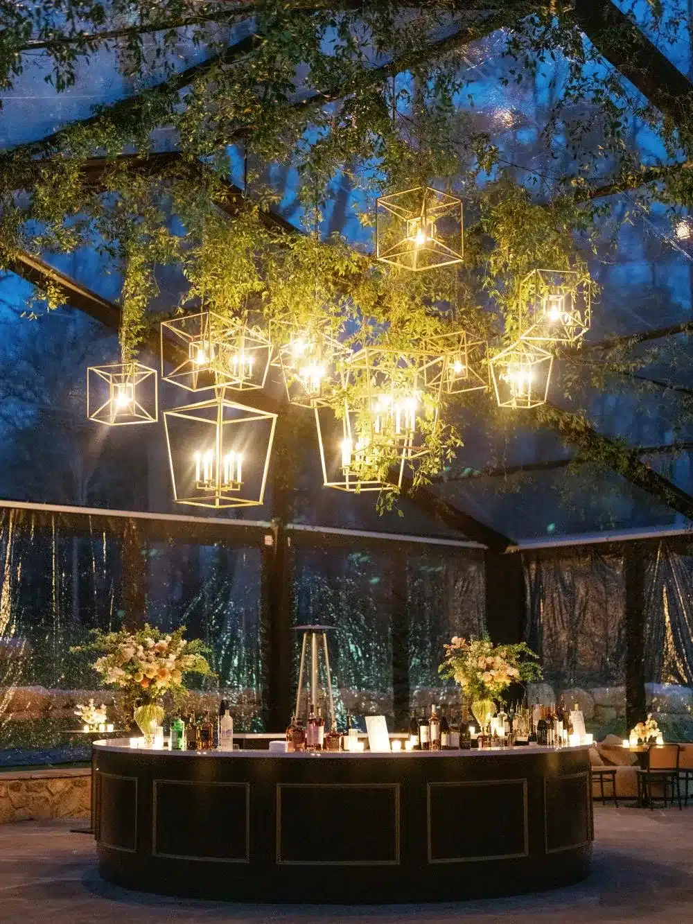 Evening shot of bar under clear tent with hanging lights and greenery