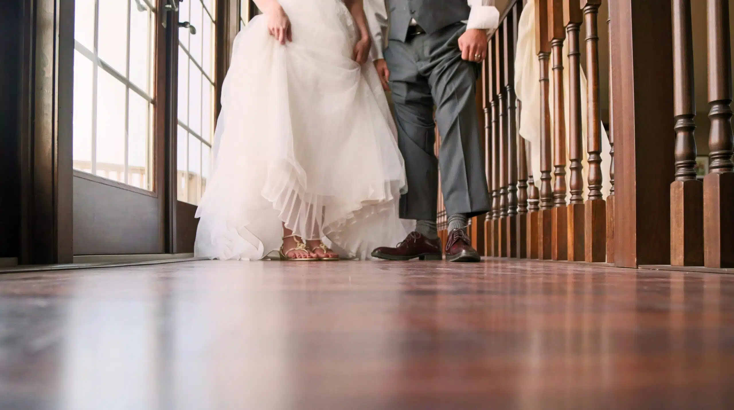 A bride and groom walk across a polished wooden floor, showcasing a charming and unique flooring choice that adds warmth and elegance to the wedding venue.