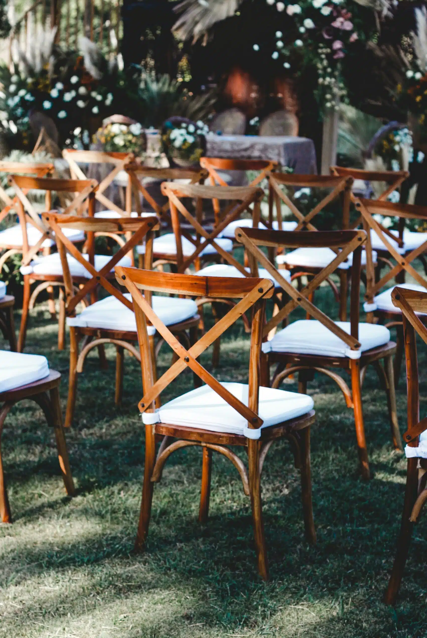 Rows of wooden cross-back chairs with white cushions arranged on grass, creating a comfortable and accessible wedding ceremony layout.