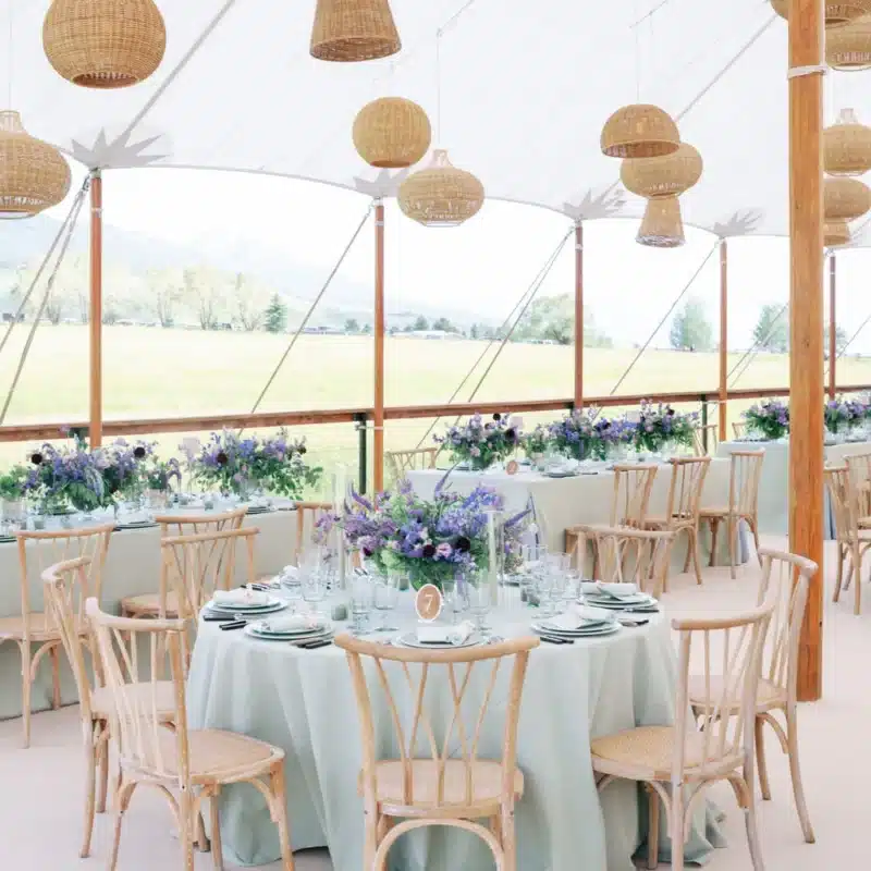 Elegant sailcloth tent setup with woven pendant lighting and floral centerpieces.