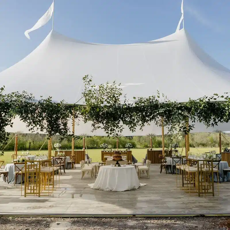 Open-sided wedding tent with greenery and round tables on a wooden floor.