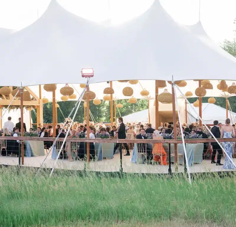 Daytime wedding under a sailcloth tent with woven rattan pendant lights and scenic surroundings