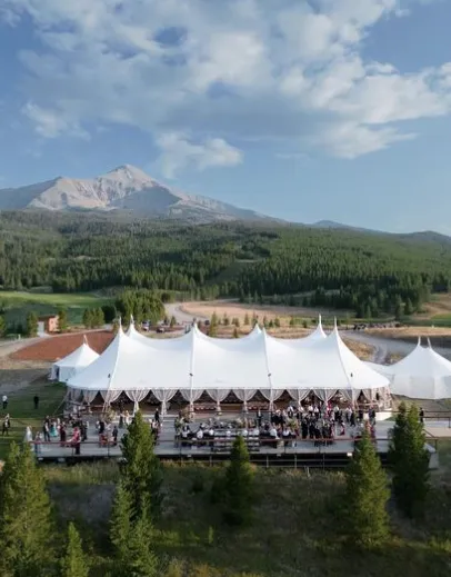 Large sailcloth tent set against a mountainous backdrop, showcasing its aerodynamic peaks and durable structure designed to withstand varied weather conditions like wind and rain.