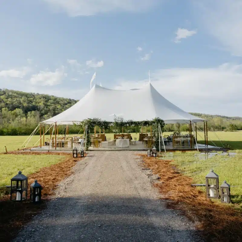 Daytime view of an open-sided sailcloth tent set in a grassy field, illustrating effective ventilation techniques that help maintain interior dryness and reduce condensation.