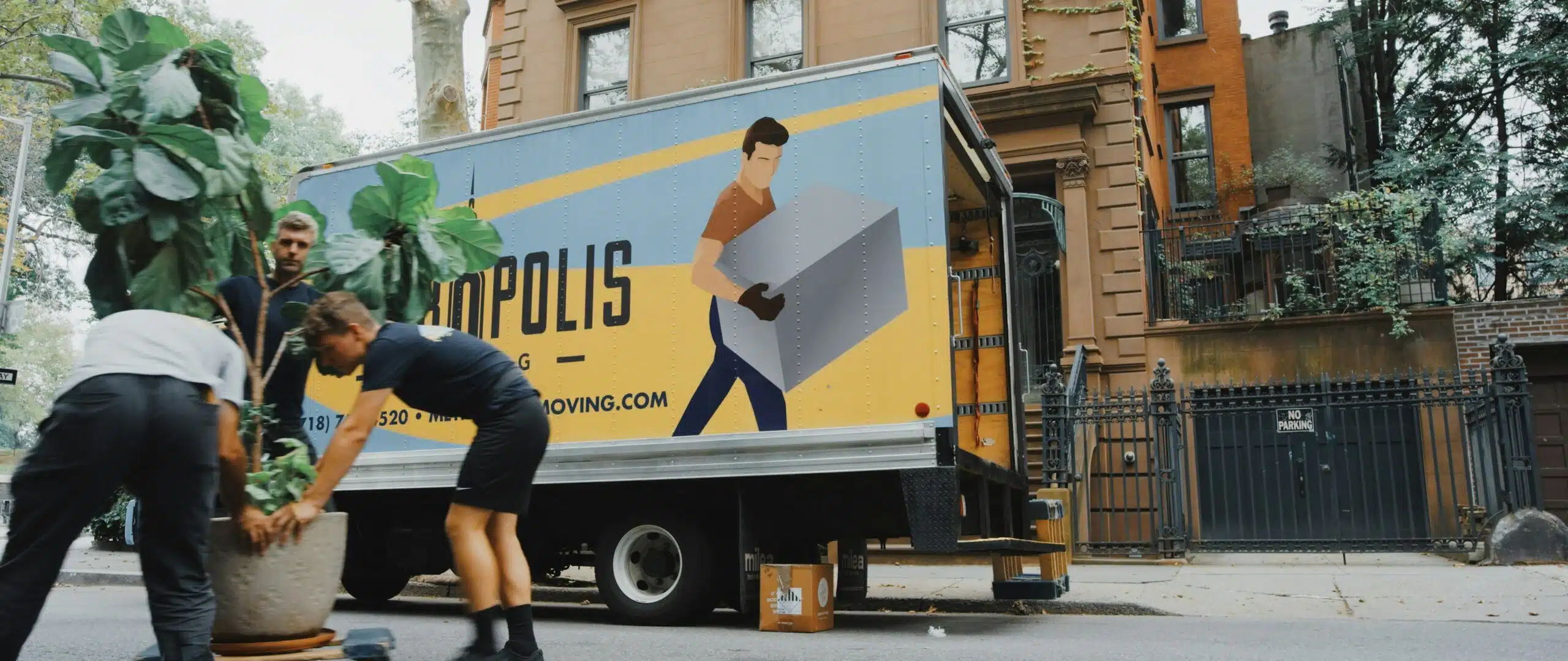 Crew members work together to load a heavy plant into a moving truck, illustrating the higher manpower typically required for setting up sailcloth tents compared to frame tents. 