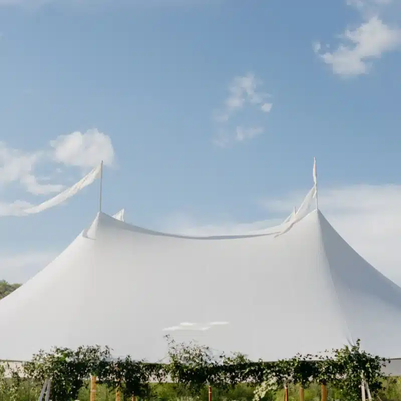 A pristine sailcloth tent with elegant peaks and flowing flags, showcasing its durable structure and professional installation ideal for outdoor event rentals.