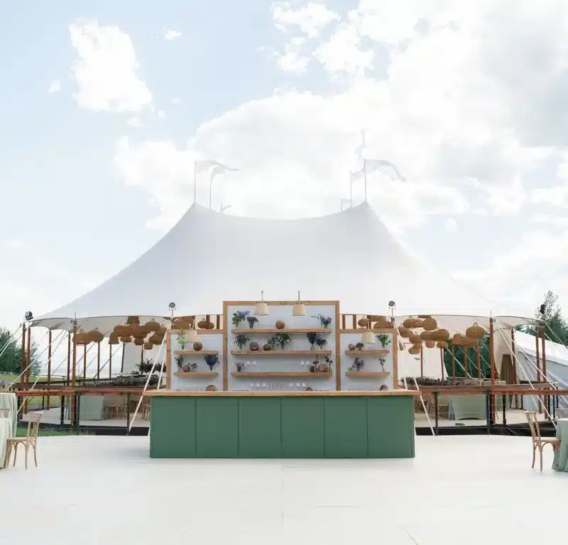 Modern outdoor bar setup with open shelving in front of a grand Century Pole Tent at a wedding or event.