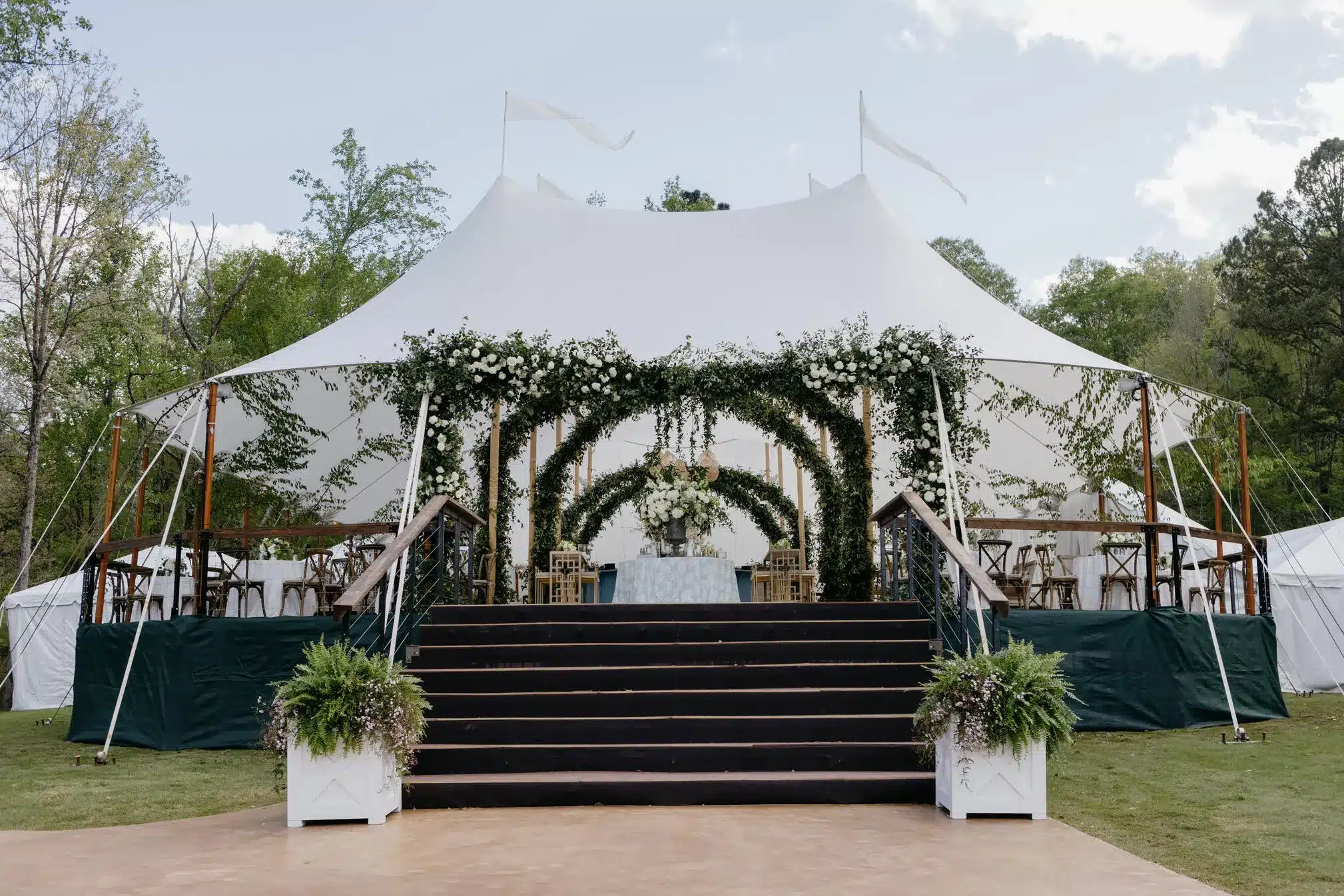 Elevated flooring, floral entry arches, and secured rigging illustrate essential event infrastructure for Century Pole Tents that enhances safety and upscale presentation.