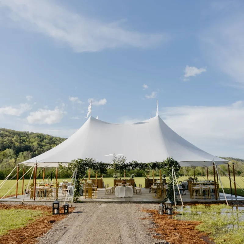 Century Pole Tent securely staked on a wooden platform in an open field, showcasing weather resistance and wind durability benefits over frame tents.