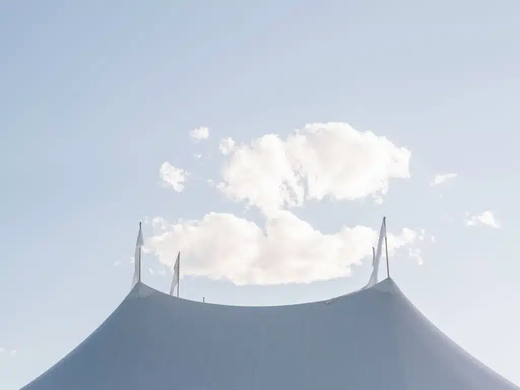 Top of a white event tent against a blue sky with clouds