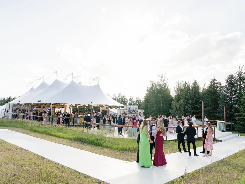 Guests mingling outside a large white event tent on a sunny day