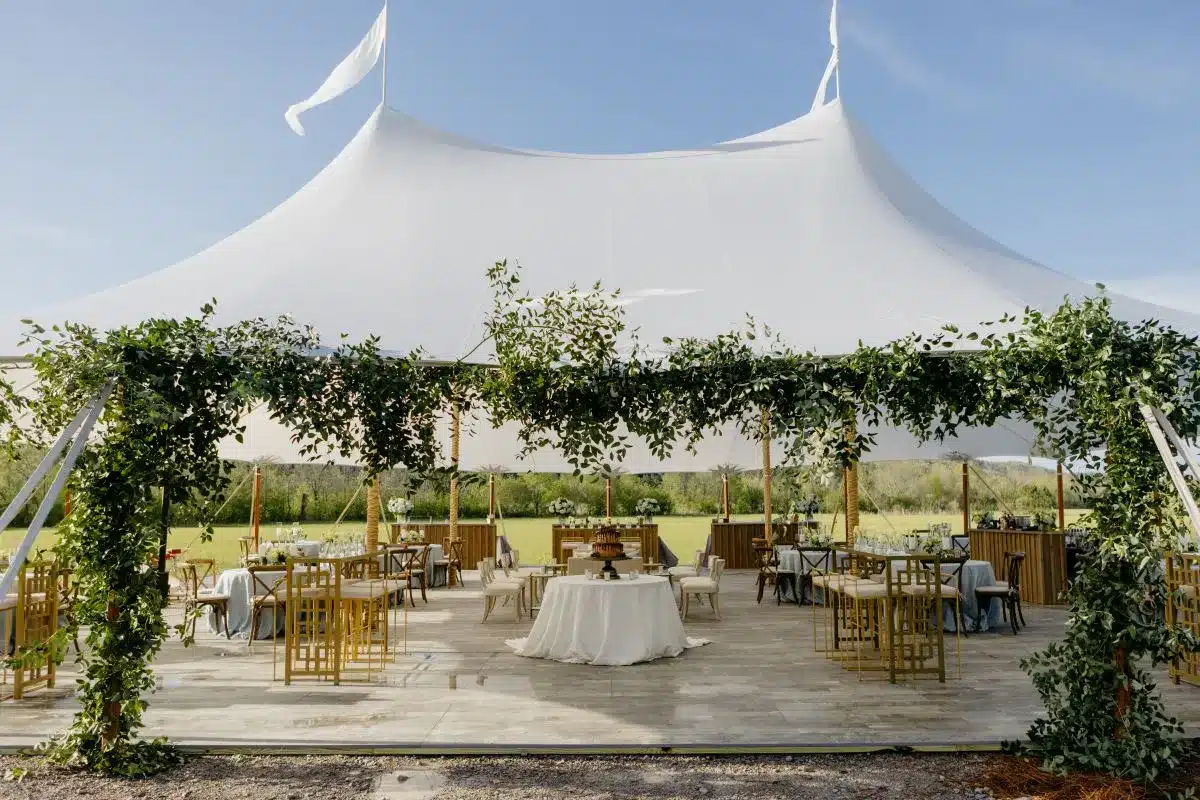 Interior of a high peak tent with wooden chairs and greenery accents.