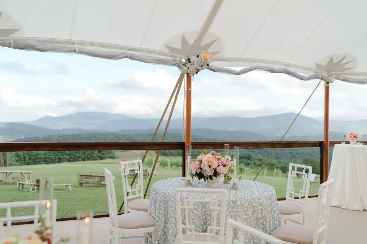 Round table with floral centerpiece under a high peak tent overlooking mountains.