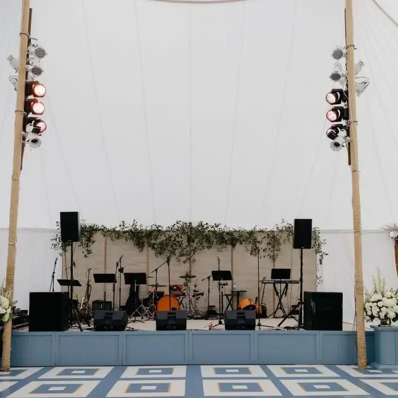 Century Pole Tent interior with elevated stage, audio equipment, and floral décor for live event setup.