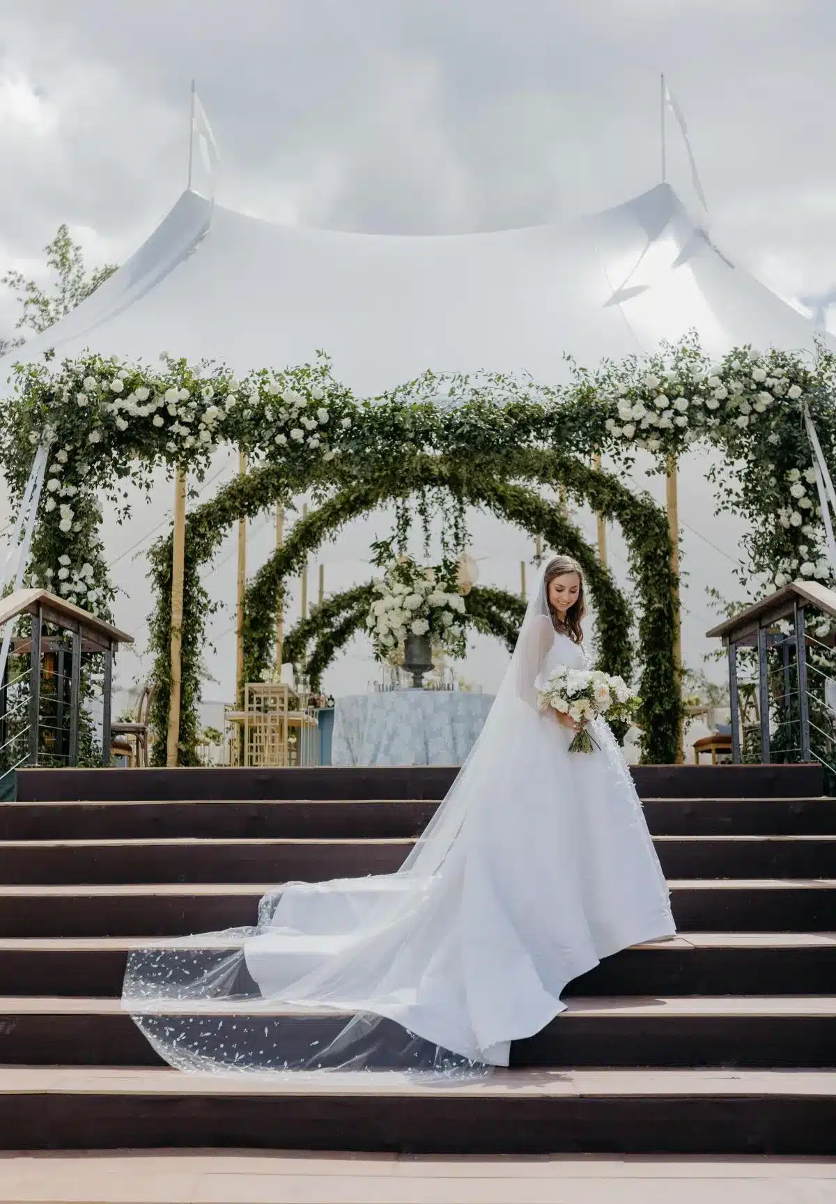Bride in front of a floral arch entrance under a high peak wedding tent.