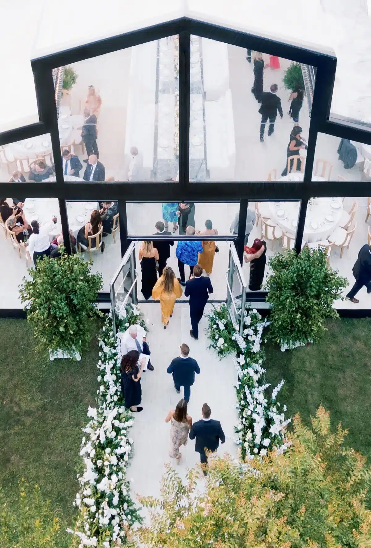 Guests entering a clear span tent decorated with greenery and flowers.