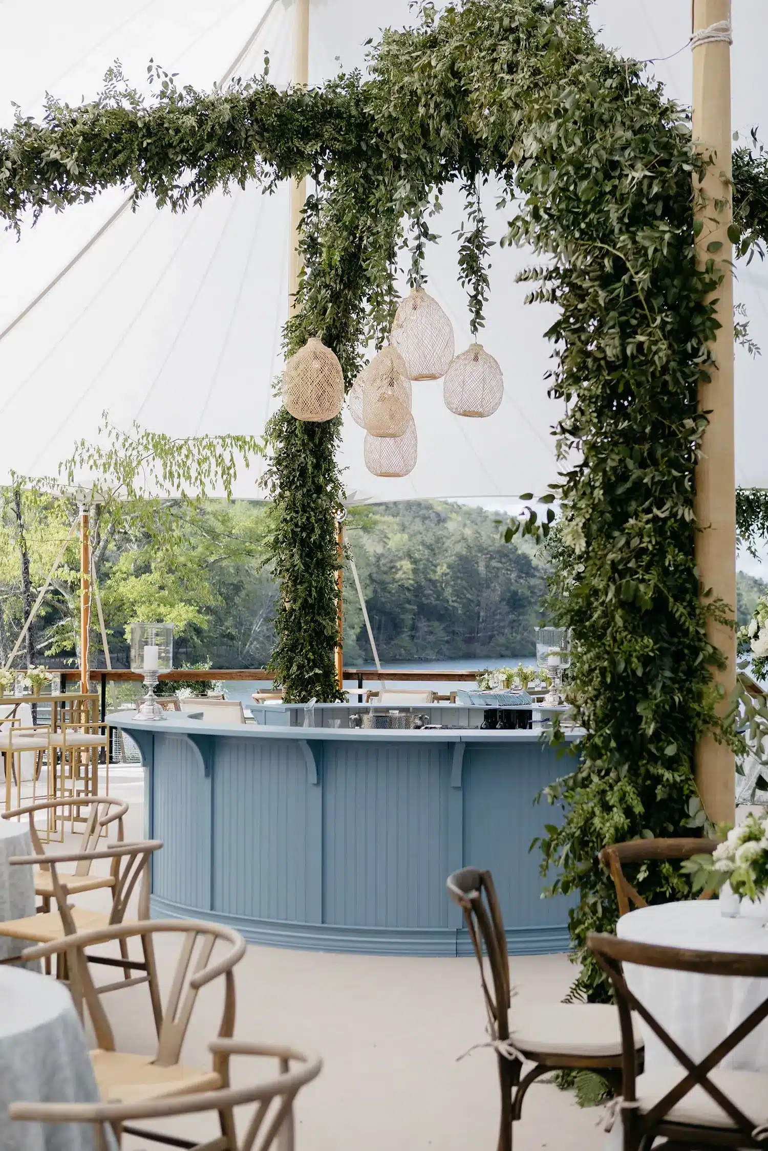 Blue circular bar beneath greenery arch and woven pendant lights inside a Century Pole Tent.