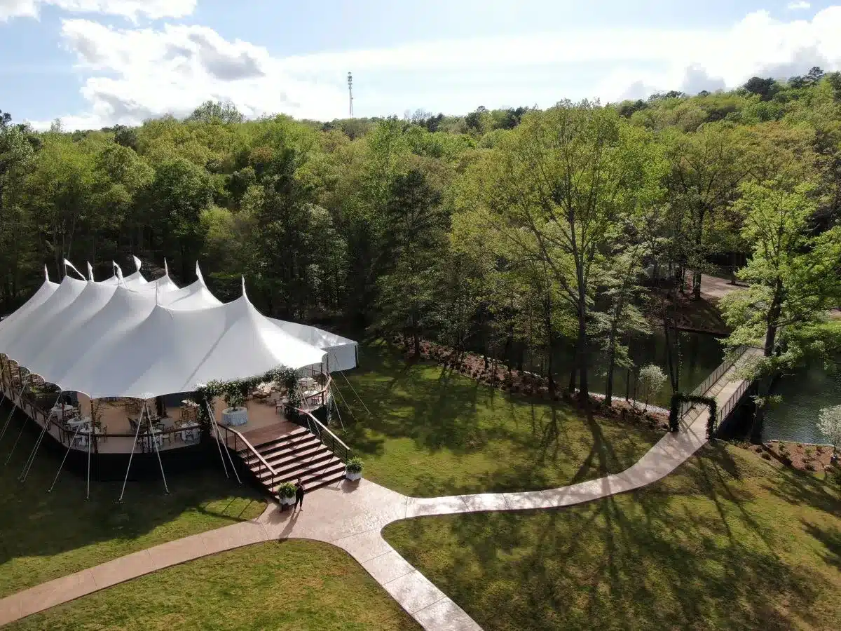 Sailcloth tent set up on a lush lawn beside a wooded pond