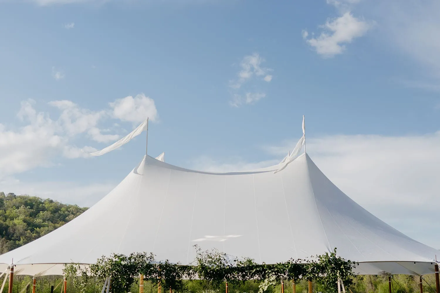 White high peak tent set up outdoors against blue sky.
