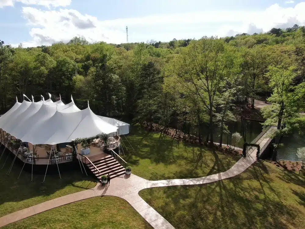 Spacious sailcloth tent with elevated flooring and floral décor, showcasing customizable options like layout, staging, and scenic venue integration for corporate events.