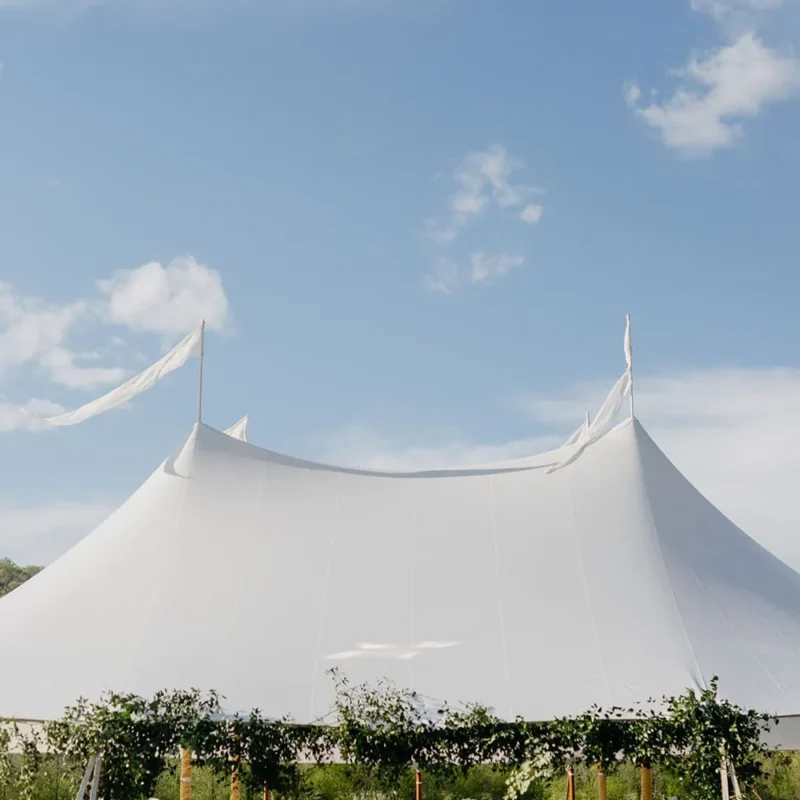 Sailcloth event tent with high peaks and flowing flags under a blue sky.