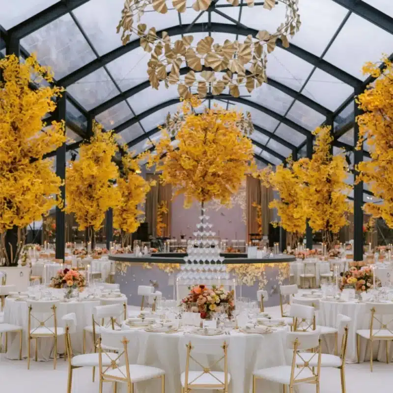 Seasonal tent interior with autumn-themed golden trees and elegant dining tables
