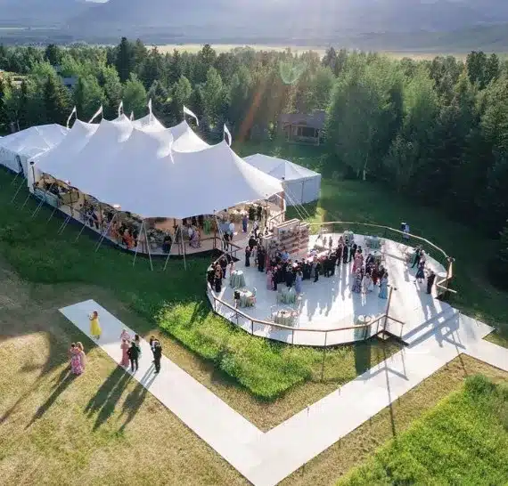 Aerial view of a large sailcloth tent with an adjacent outdoor cocktail lounge and guest mingling area.