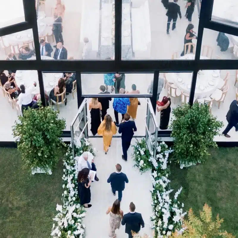 Guests entering a clear glass tent with floral-lined flooring path
