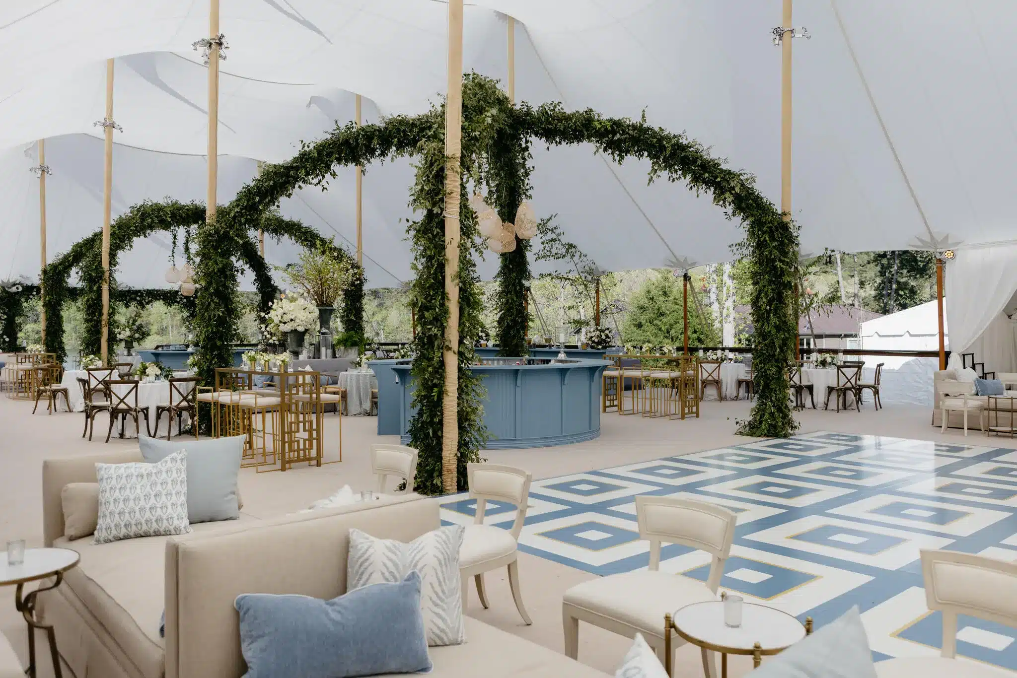 Elegant corporate event setup under a sailcloth tent with luxe furnishings, greenery, and a geometric dance floor—highlighting the premium appeal of tented venues.