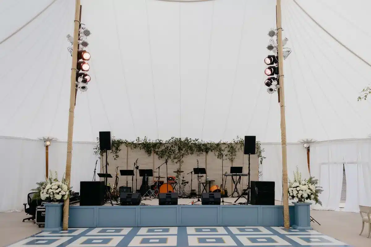 Indoor stage with instruments and floral backdrop inside a sailcloth event tent.