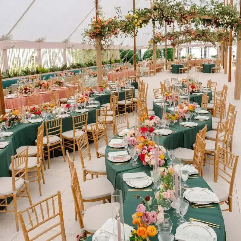 Vibrant wedding reception with green and pink table linens under a floral-draped tent.
