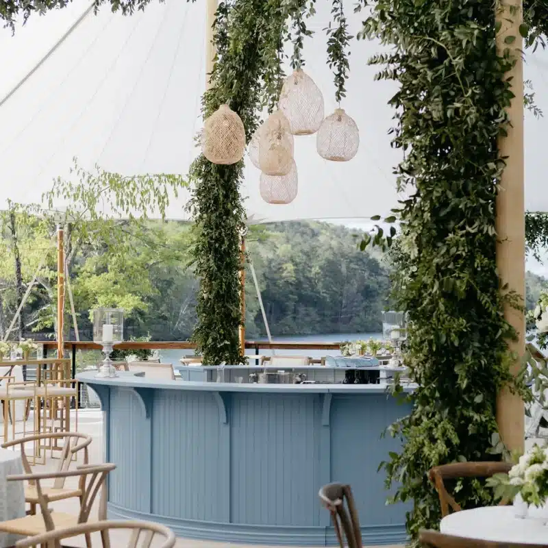 Round bar under tent canopy, decorated with lush greenery and woven pendant light fixtures.