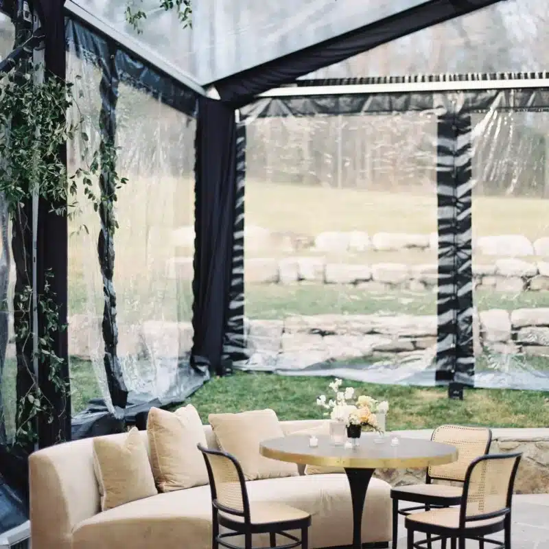 Cozy lounge area inside a clear tent with modern seating and small floral accents.