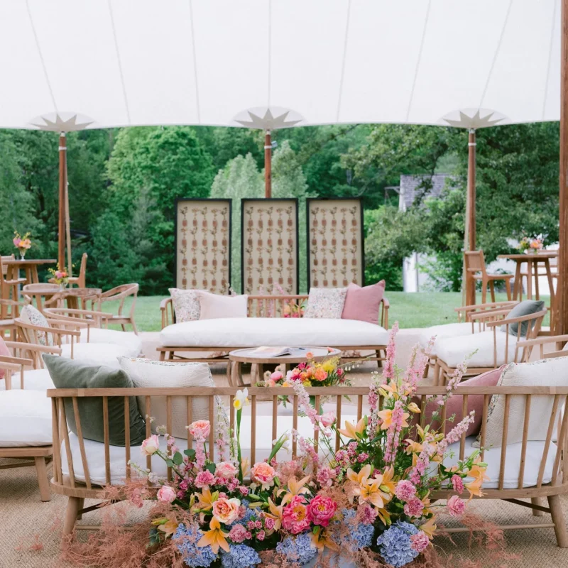 Outdoor lounge seating with colorful floral arrangements under a tent.