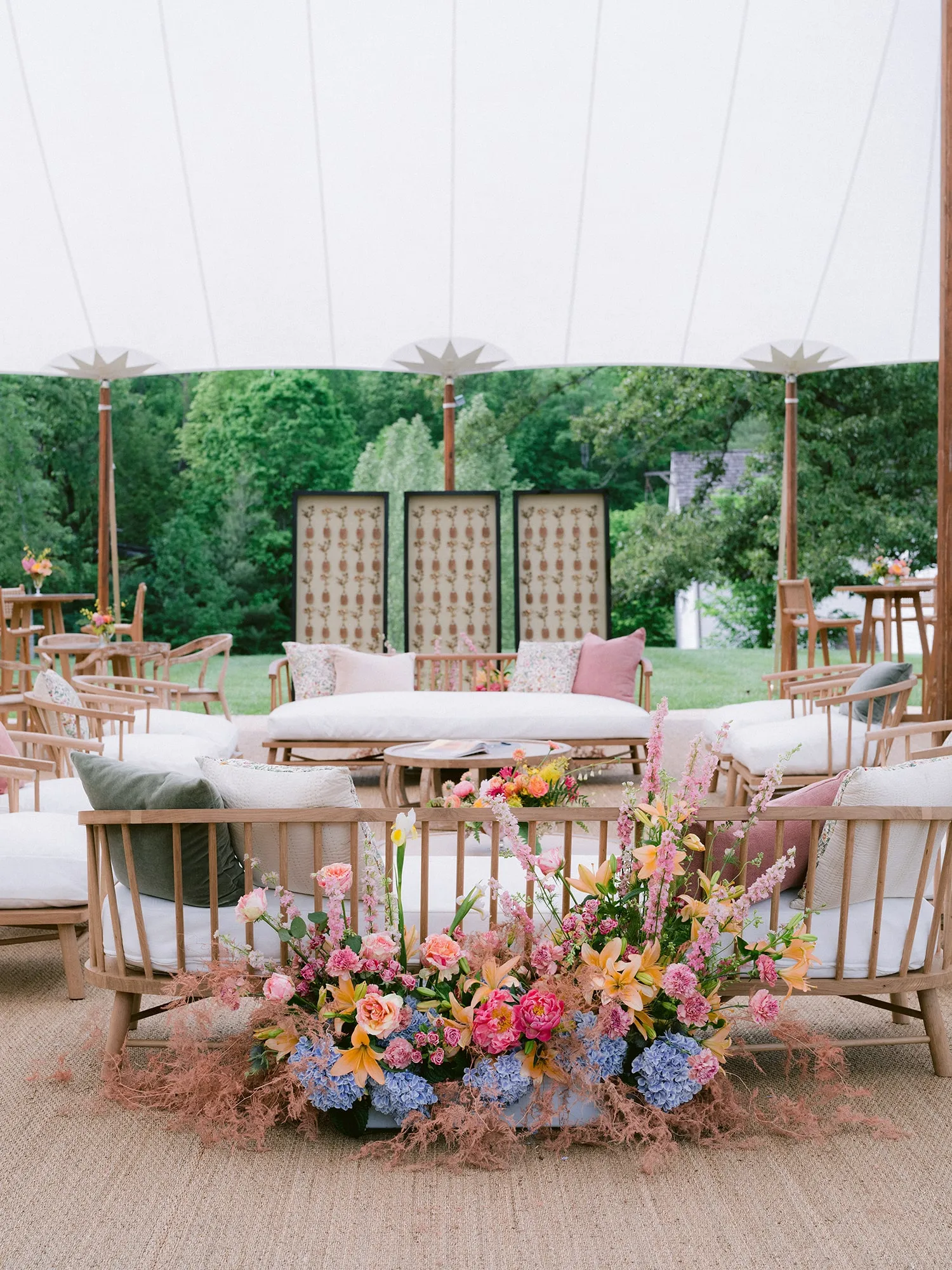 Outdoor lounge seating with colorful floral arrangements under a tent.
