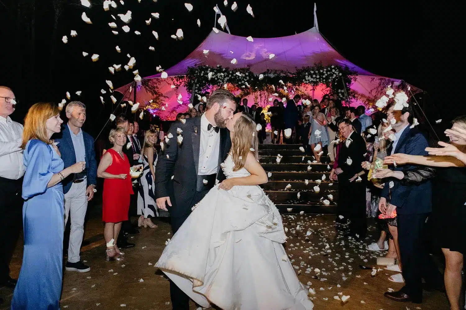 Bride and groom kissing under a tent with floral and lighting décor at night