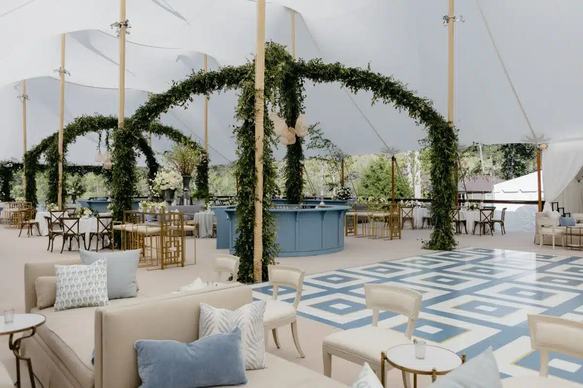 Tent interior with patterned dance floor, lounge seating, and greenery arches.