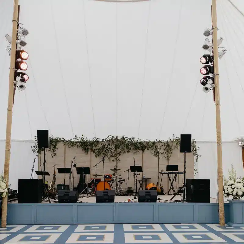 Wedding tent stage with musical instruments, lighting, and floral décor