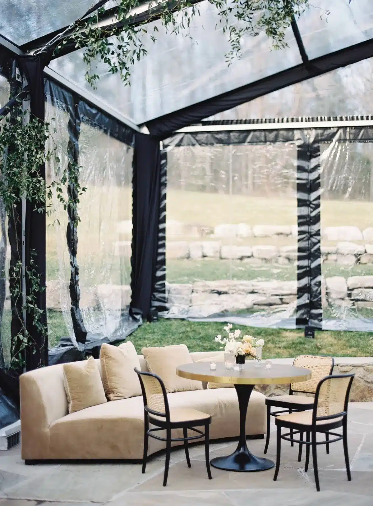 Cozy lounge area inside a clear tent with beige sofa and round table.