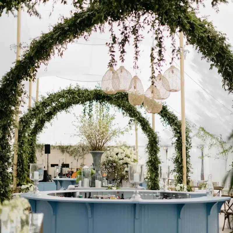 Blue circular bar under tent with greenery arches and woven pendant lights.